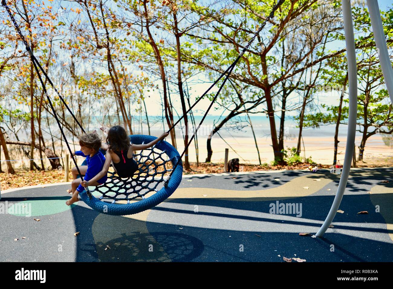 Two children playing on a nest swing, Balgal beach, QLD, Australia Stock Photo
