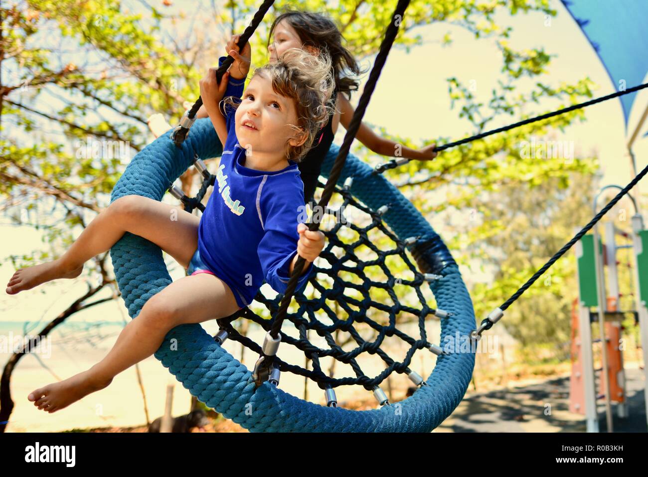 Two children playing on a nest swing, Balgal beach, QLD, Australia Stock Photo
