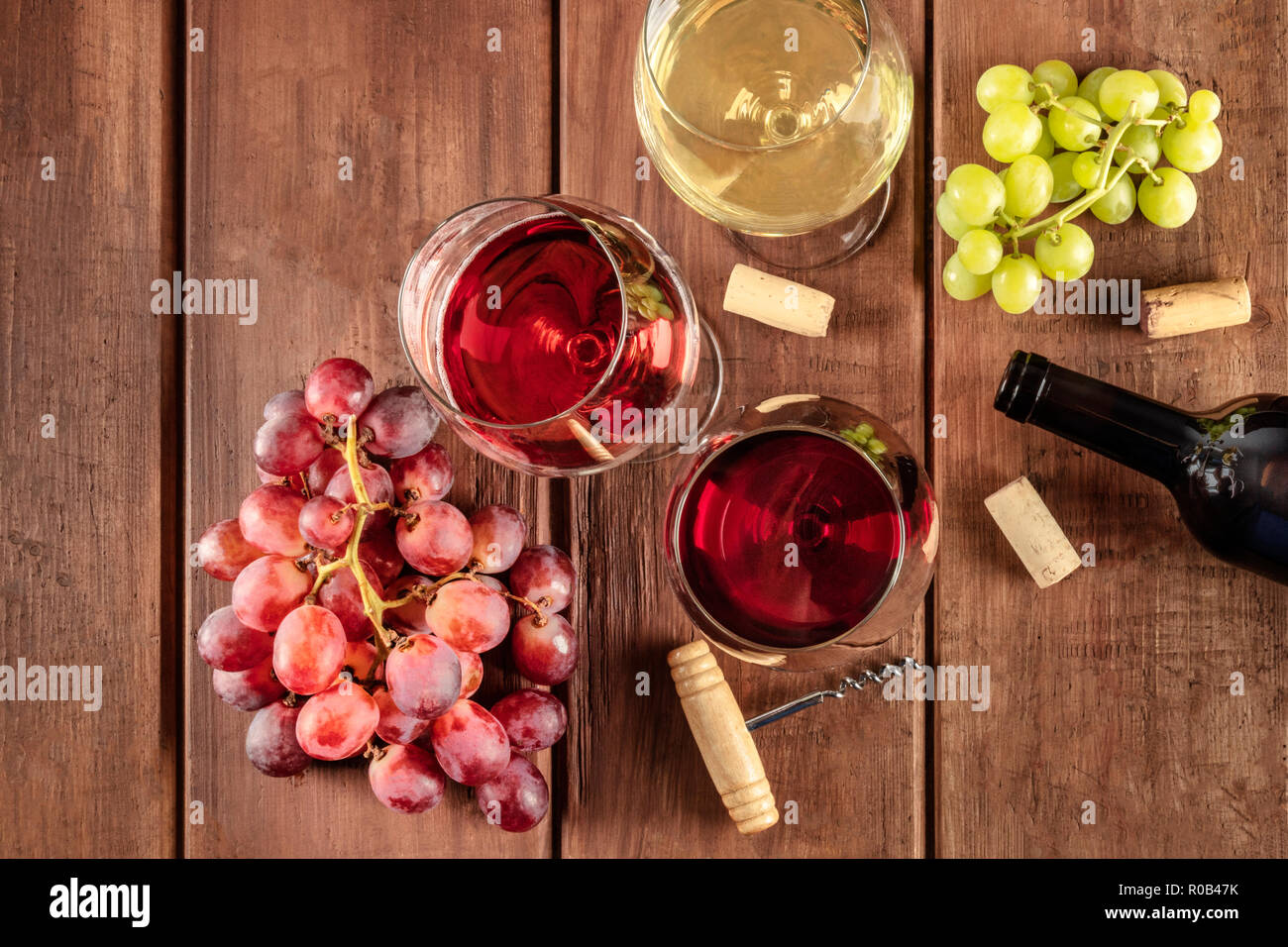 Retro Cellar Wine Tasting. Glasses of red, rose, and white wine with a bottle, grapes, and a vintage corkscew and corks, shot from the top Stock Photo