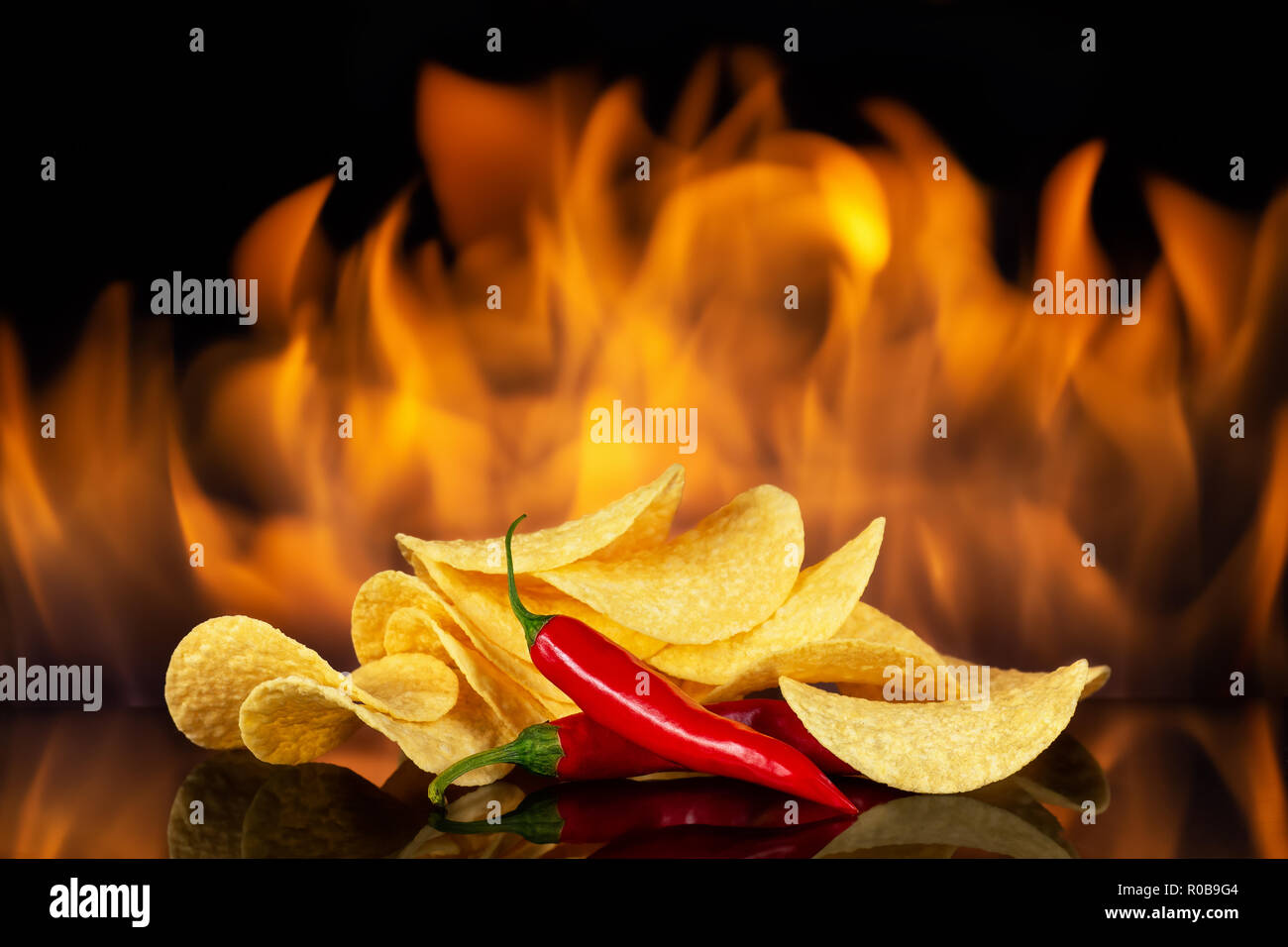 heap of spicy potato chips with chili pepper on fire background Stock