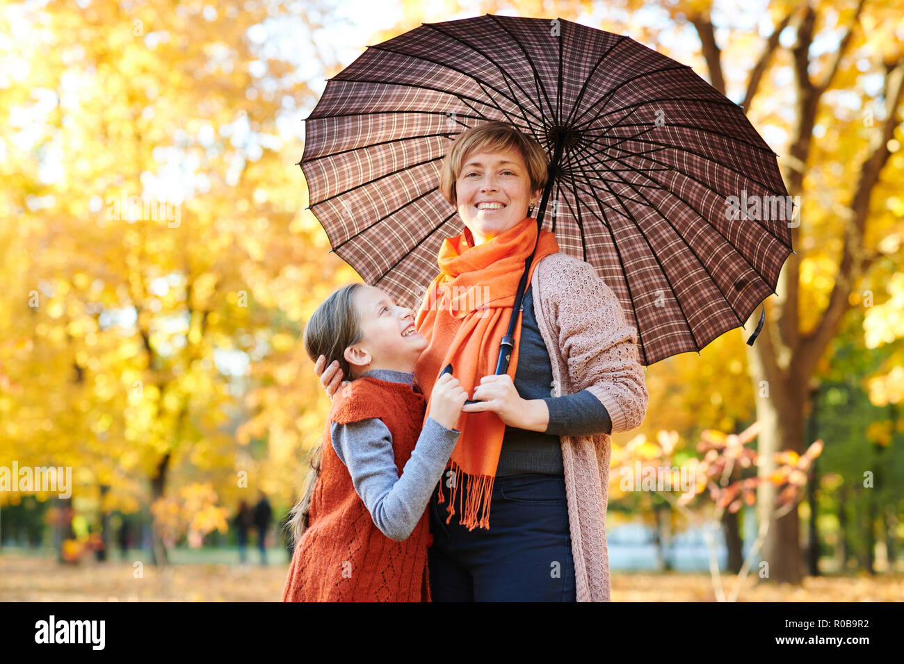 Mother and daughter are in autumn city park. Peoples are posing under ...