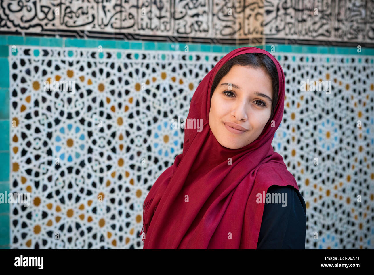 Muslim woman in traditional clothing with red hijab and black dress in front of traditional arabesque decorated wall Stock Photo