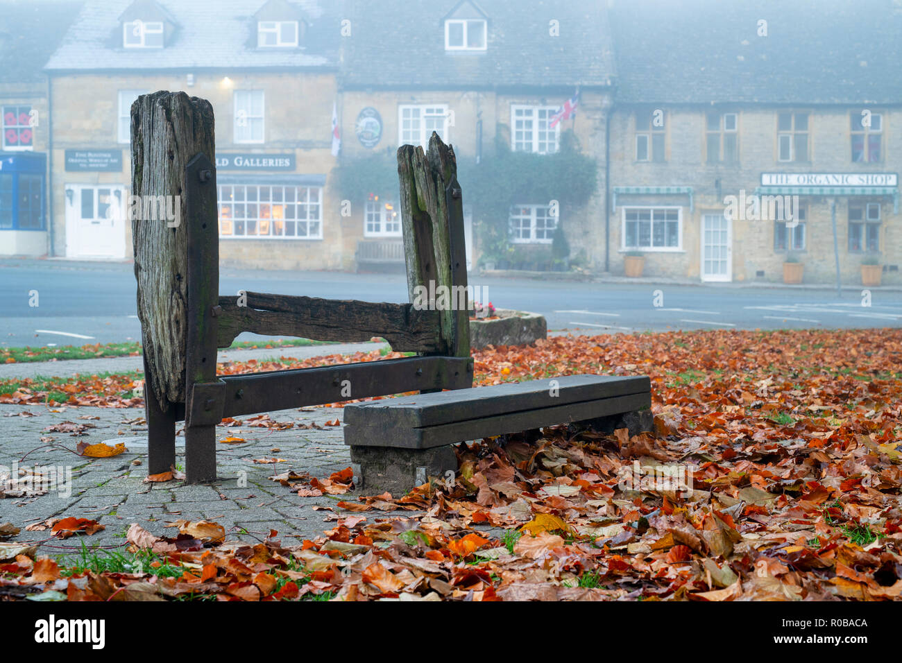 The village penal stocks on the green in the early morning autumn fog, Stow on the Wold, Gloucestershire, Cotswolds, England Stock Photo