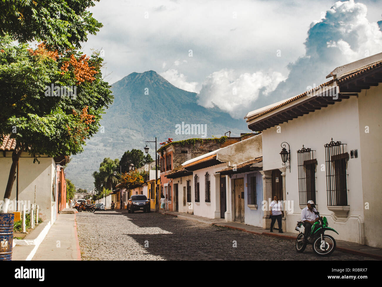 Typical cobbled street in Antigua Guatemala during a sunny day - Volcan Agua volcano looming over colonial style houses Stock Photo