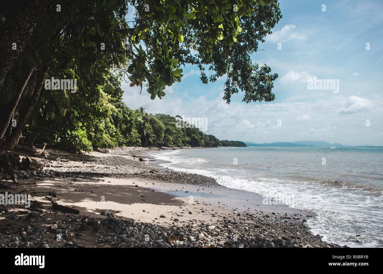 Dense forest gives way to a dark stony beach on the cape of the Nicoya Peninsula in Costa Rica, near Manzanillo Stock Photo