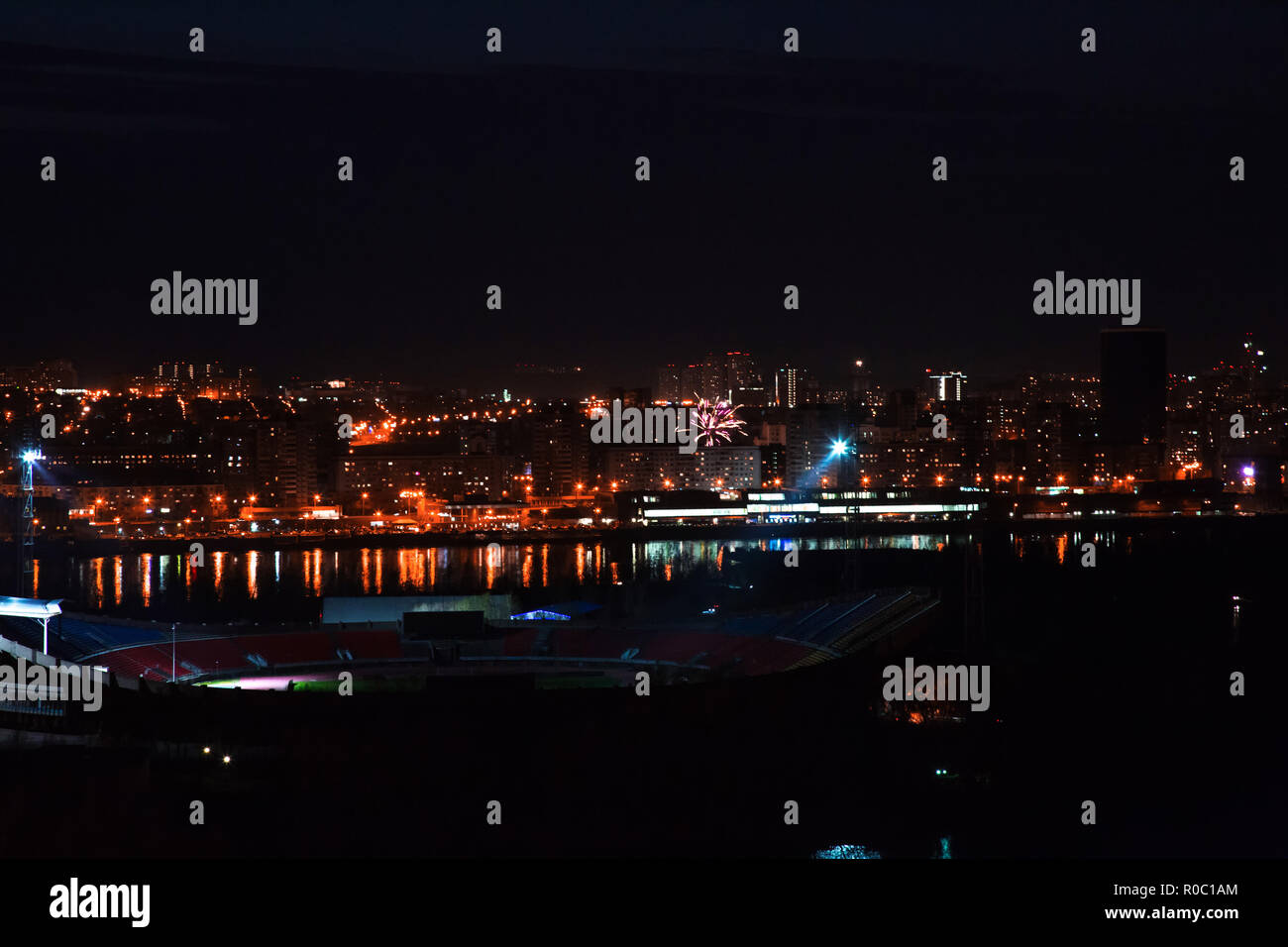 Photo views of the night city of Krasnoyarsk with the lights of houses, the lights of the stadium, fireworks over the river Stock Photo