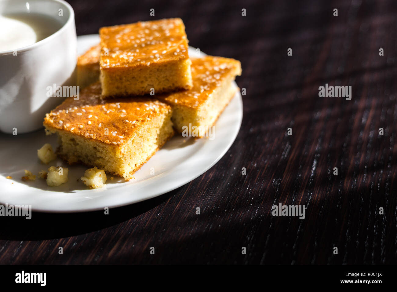 Close-up view of fresh baked corn bread with cheese and cup of yogurt in white plate on wooden table Stock Photo