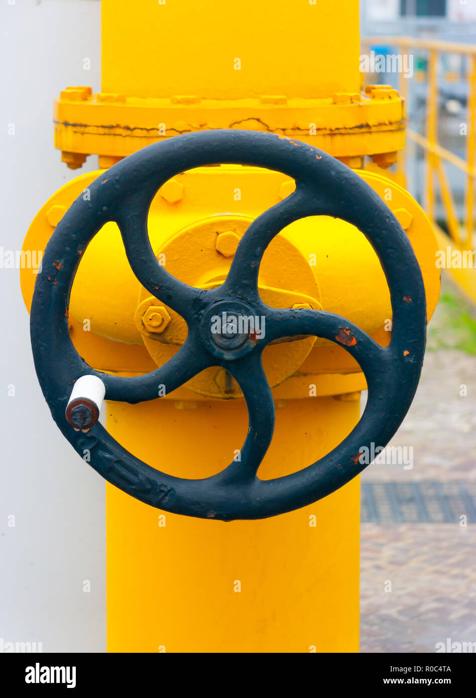 Large black manual handwheel in a control valve on a bright yellow pipe