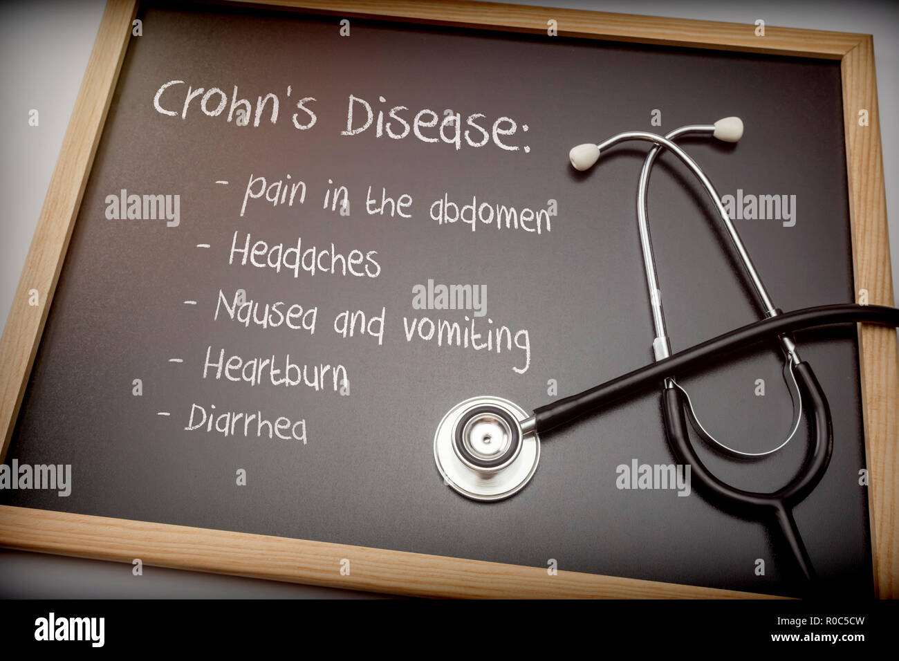 Crohn's disease can have these symptoms diarrhea, Headaches, Heartburn, Nausea and vomiting, Pain in the abdomen, Written on a blackboard next to a st Stock Photo