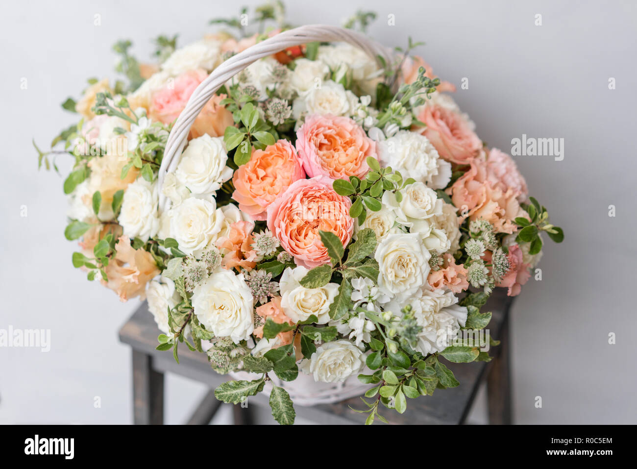 Wicker basket with mix beautiful flowers on wooden table near gray wall. Beautiful garden flowers in the arrangement , the work of a professional florist. European floral shop Stock Photo