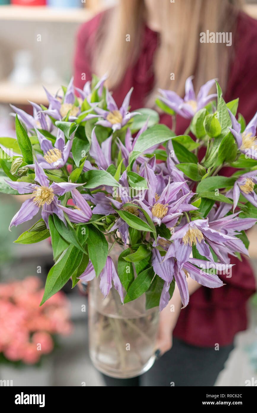 bouquet of lilac clematis flowers in glass vase. the work of the florist at  a flower shop. A glass vase with flowers placed on wooden gray table Stock  Photo - Alamy