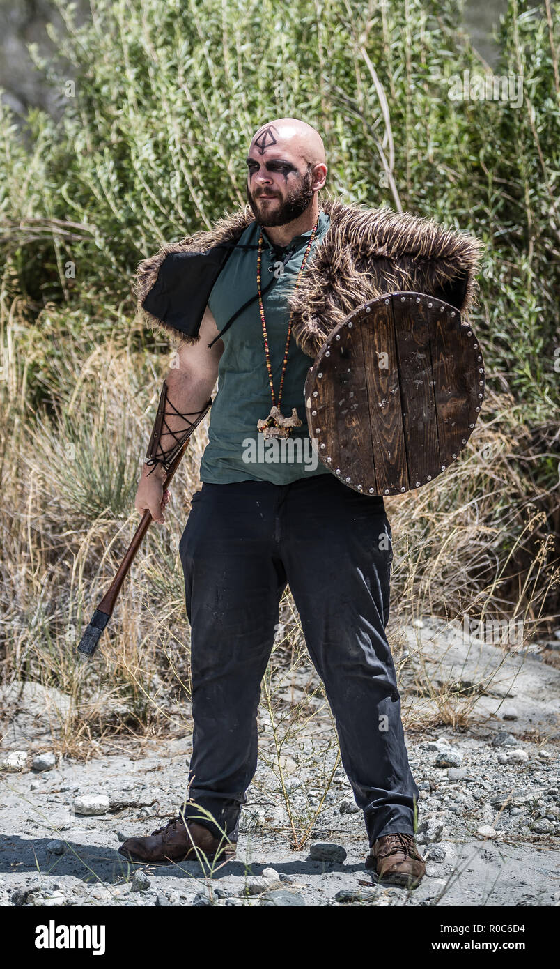 A strong caucasian male model as a viking character with axe and shield in the foothills of a large mountain. Stock Photo