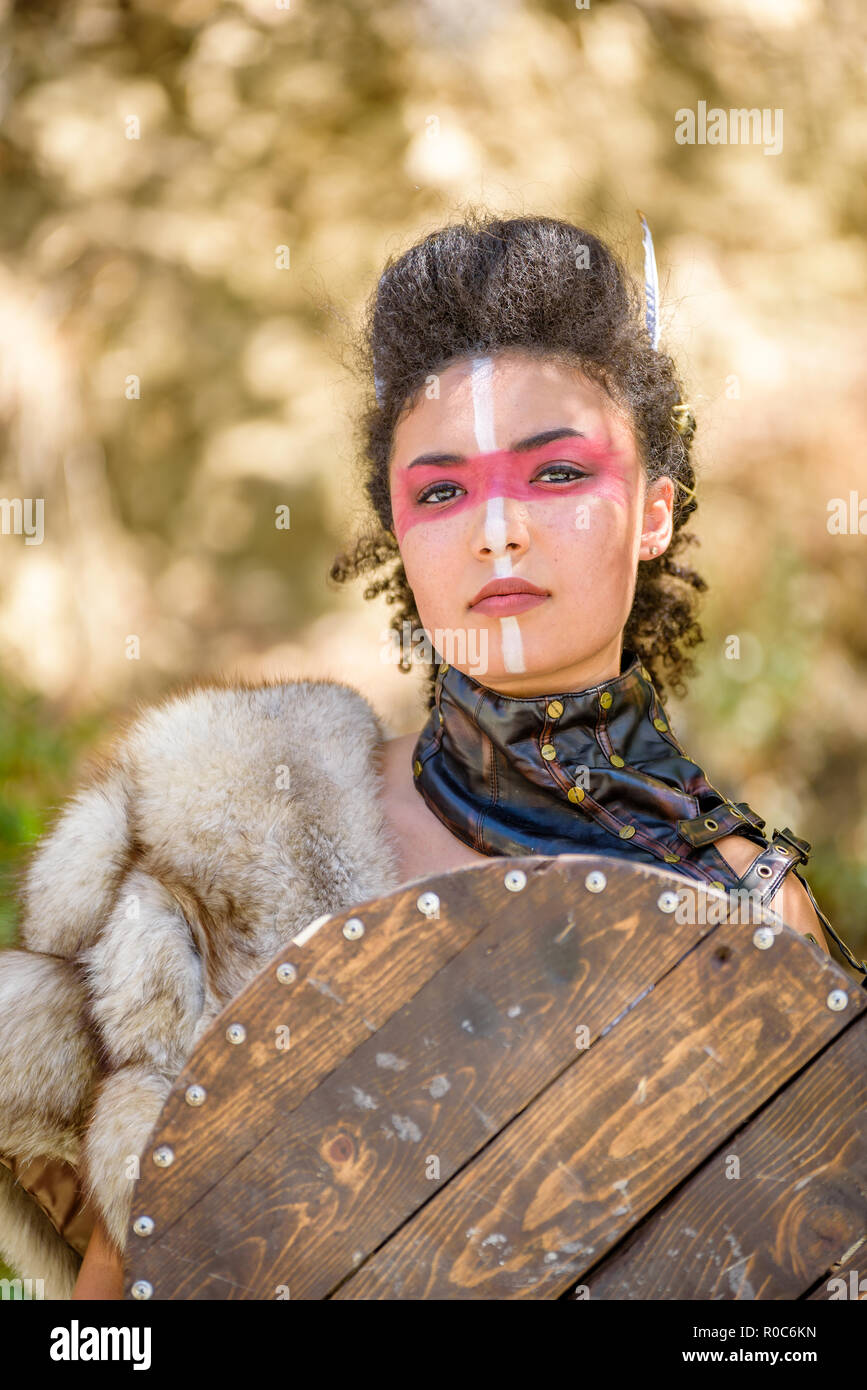 A beautiful female shield maiden character with fur and an ax in the foothills of a mountain. Fashion editorial influences Stock Photo