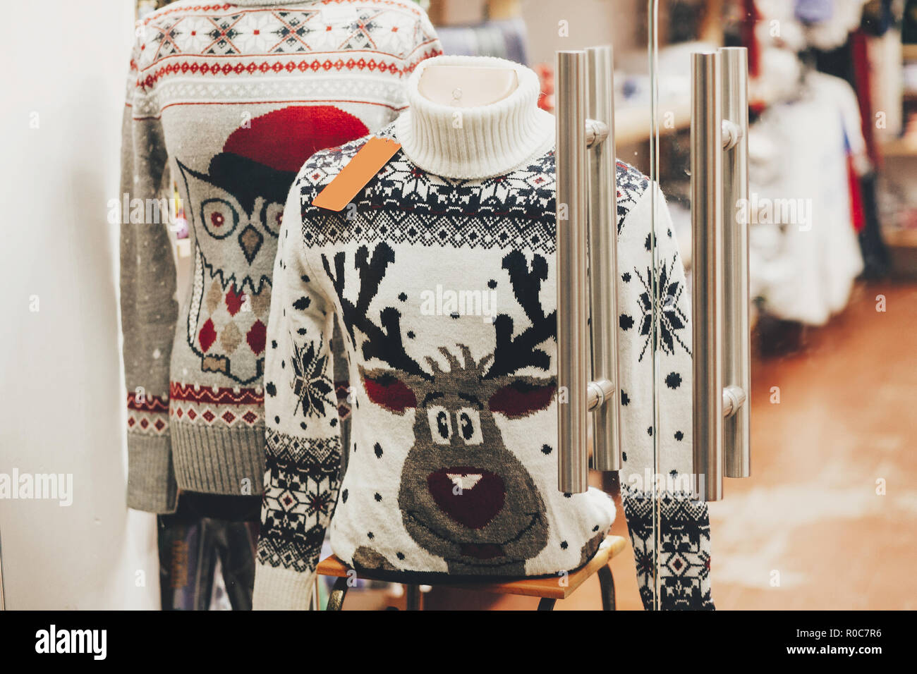Christmas sweaters with reindeer and owl in window of shop in european city street. Christmas shopping and sales. Black friday sale. Festive decoratio Stock Photo