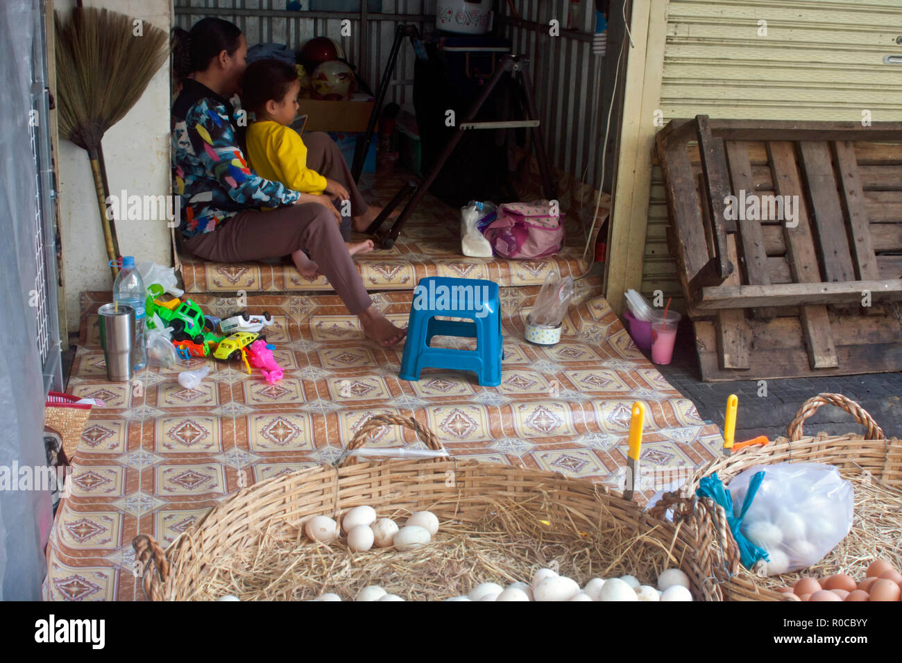 A woman is sitting with a young girl while working as an egg vendor on a city street in Phnom Penh, Cambodia. Stock Photo