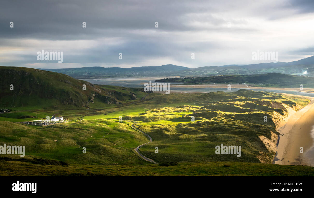 A ray of sun light breaks through the clouds to cast light on to a small white church. This is a picture of Five Finger Stand beach and sand dunes in  Stock Photo