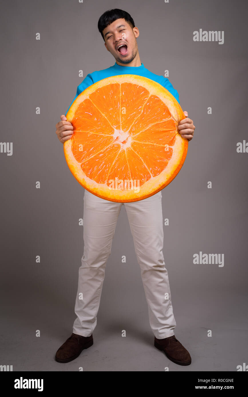 Portrait of young Asian man holding big slice of orange Stock Photo - Alamy