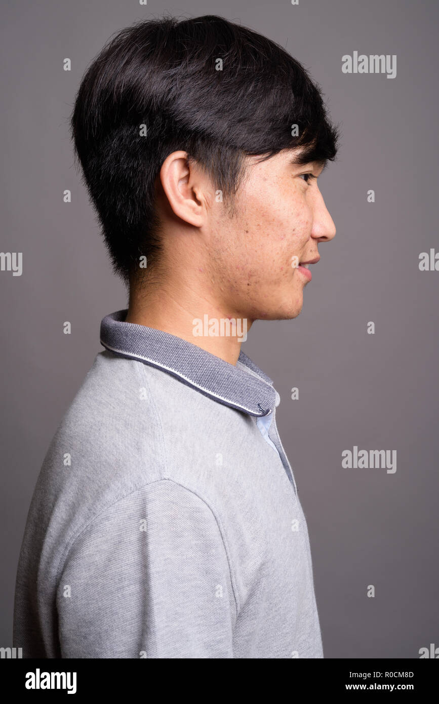 Young Asian Man Wearing Gray Polo Shirt Against Gray