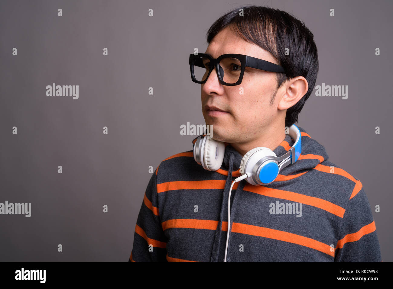 Young Asian nerd man wearing hoodie and headphones against gray  Stock Photo