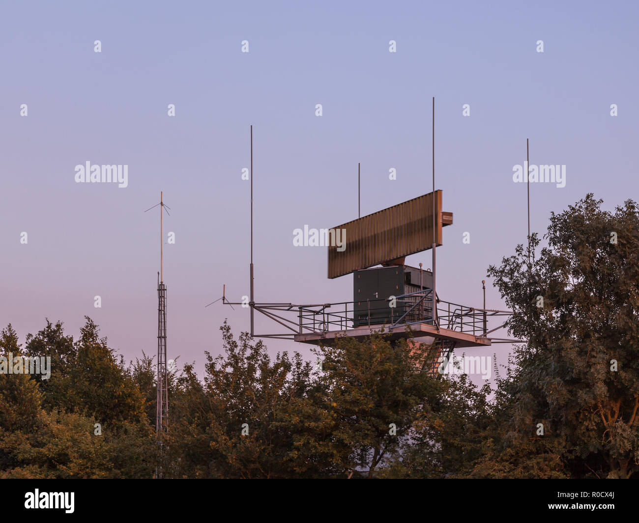 Airport radar antenna communication technology network hidden in bush during sunset. Stock Photo