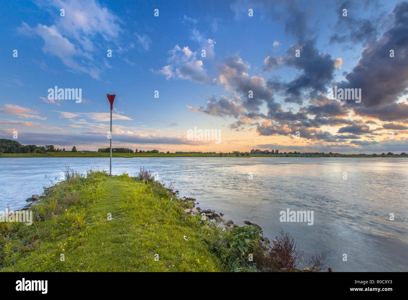 Pier preventing erosion in the river Rhine with bright blue skay and beautiful cloudscape during sunset Stock Photo