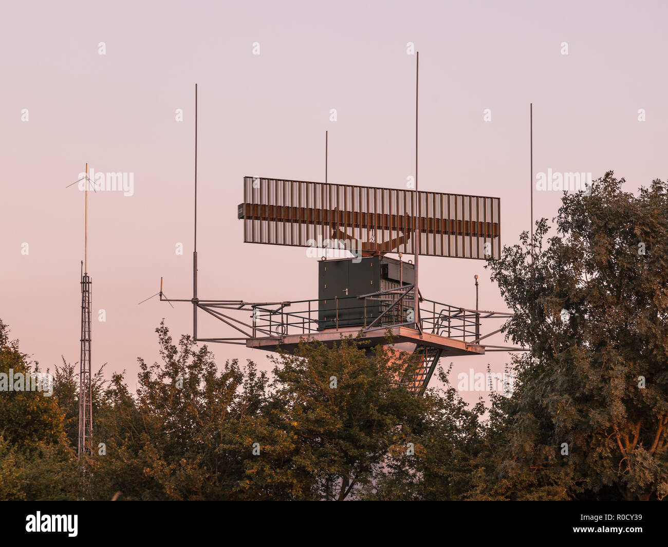 Airport radar antenna communication technology network hidden in bush during sunset. Stock Photo