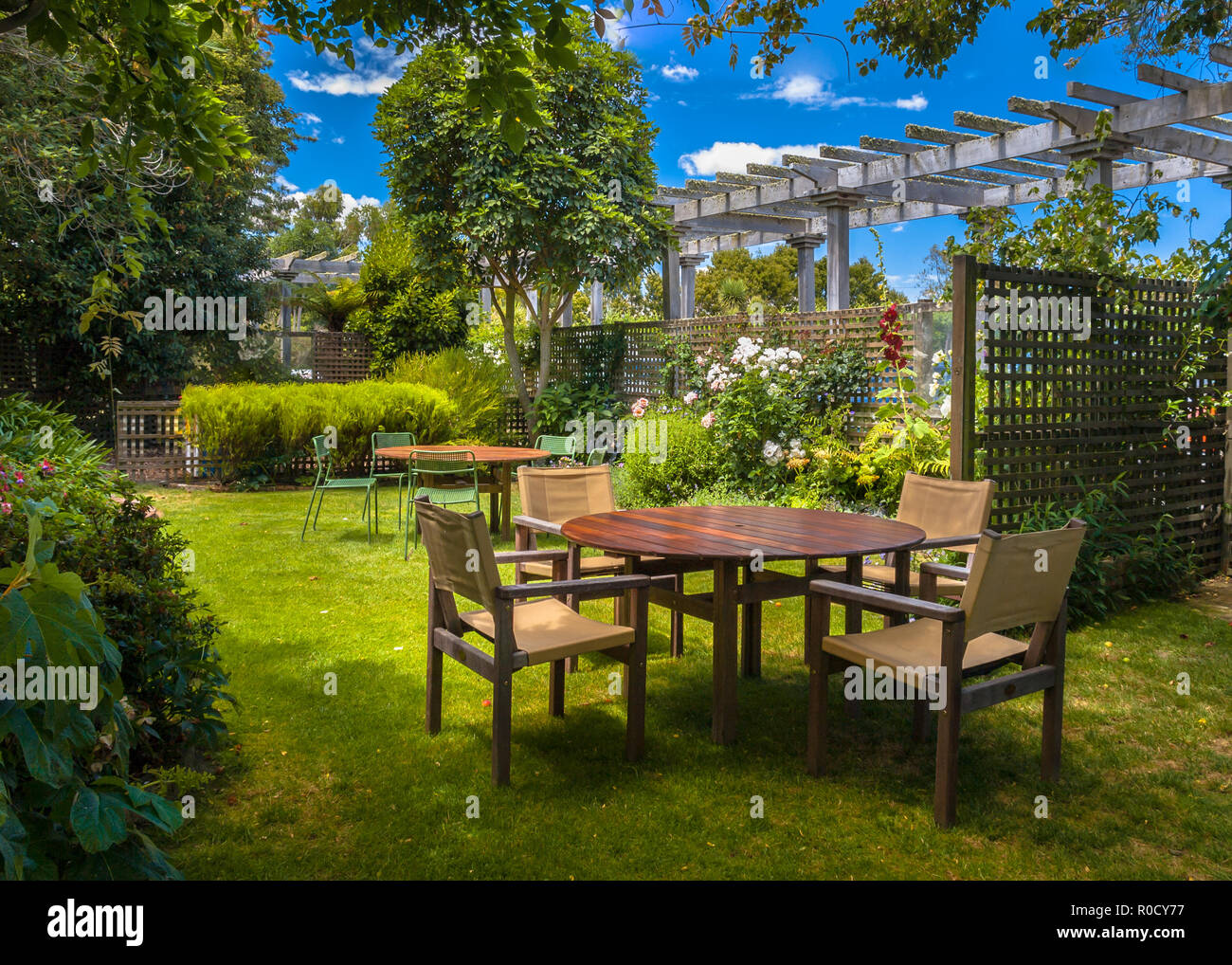 Home backyard with garden table set in sunny a lush garden with shade of trees Stock Photo