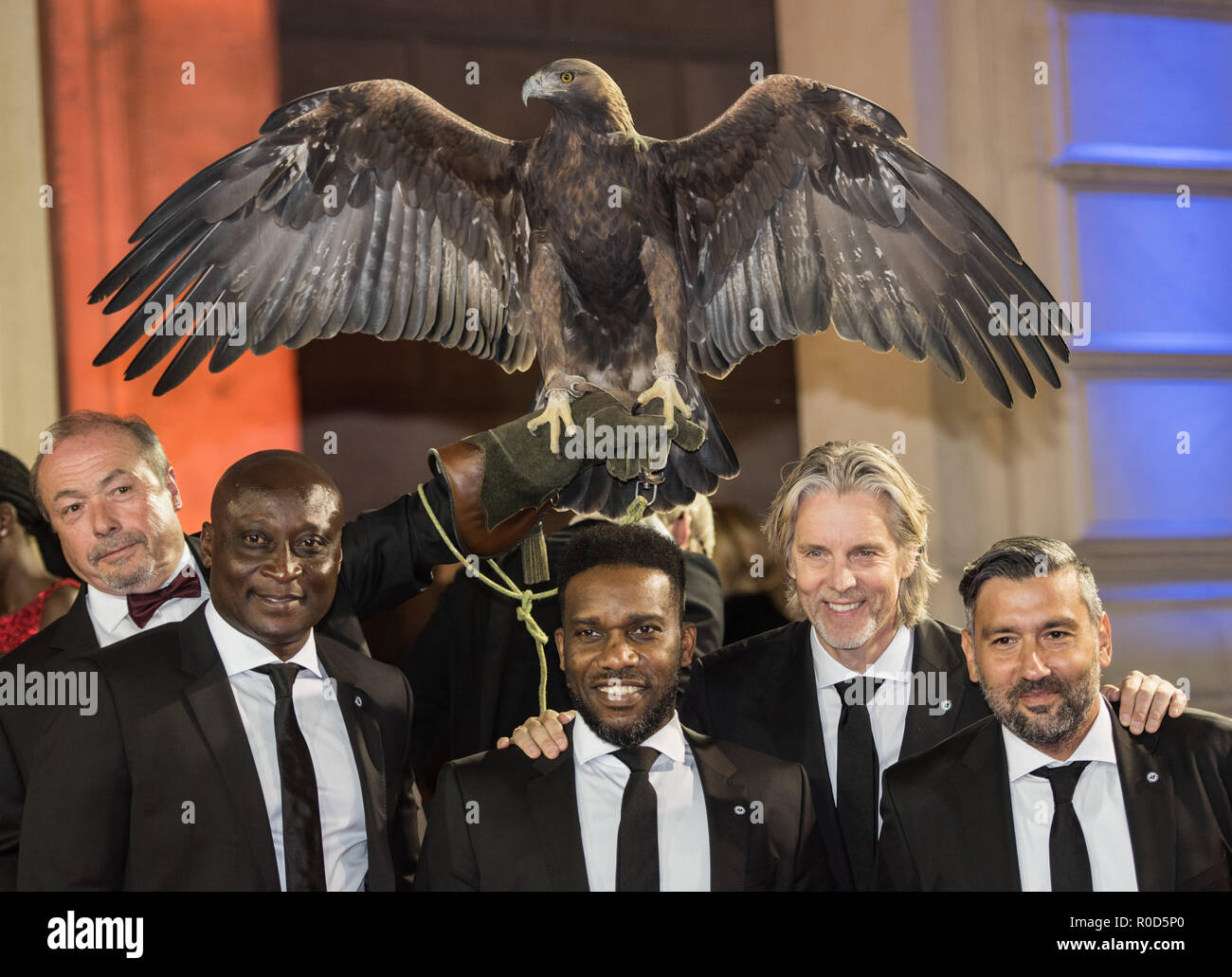 03 November 2018, Hessen, Frankfurt/Main: Anthony Yeboah (l-r, front row), Jay-Jay Okocha, Jan Aage Fjörtoft and Oka Nikolov, all former soccer players of Eintracht Frankfurt, are standing on the red carpet with Falkner Norbert Lawitschka (far left) and the Eintracht mascot, the golden eagle Attila. The 37th 'Deutsche SportpresseBall' takes place in the Alte Oper Frankfurt. One of the awards is the 'Legend of Sports' award. Photo: Andreas Arnold/dpa Stock Photo