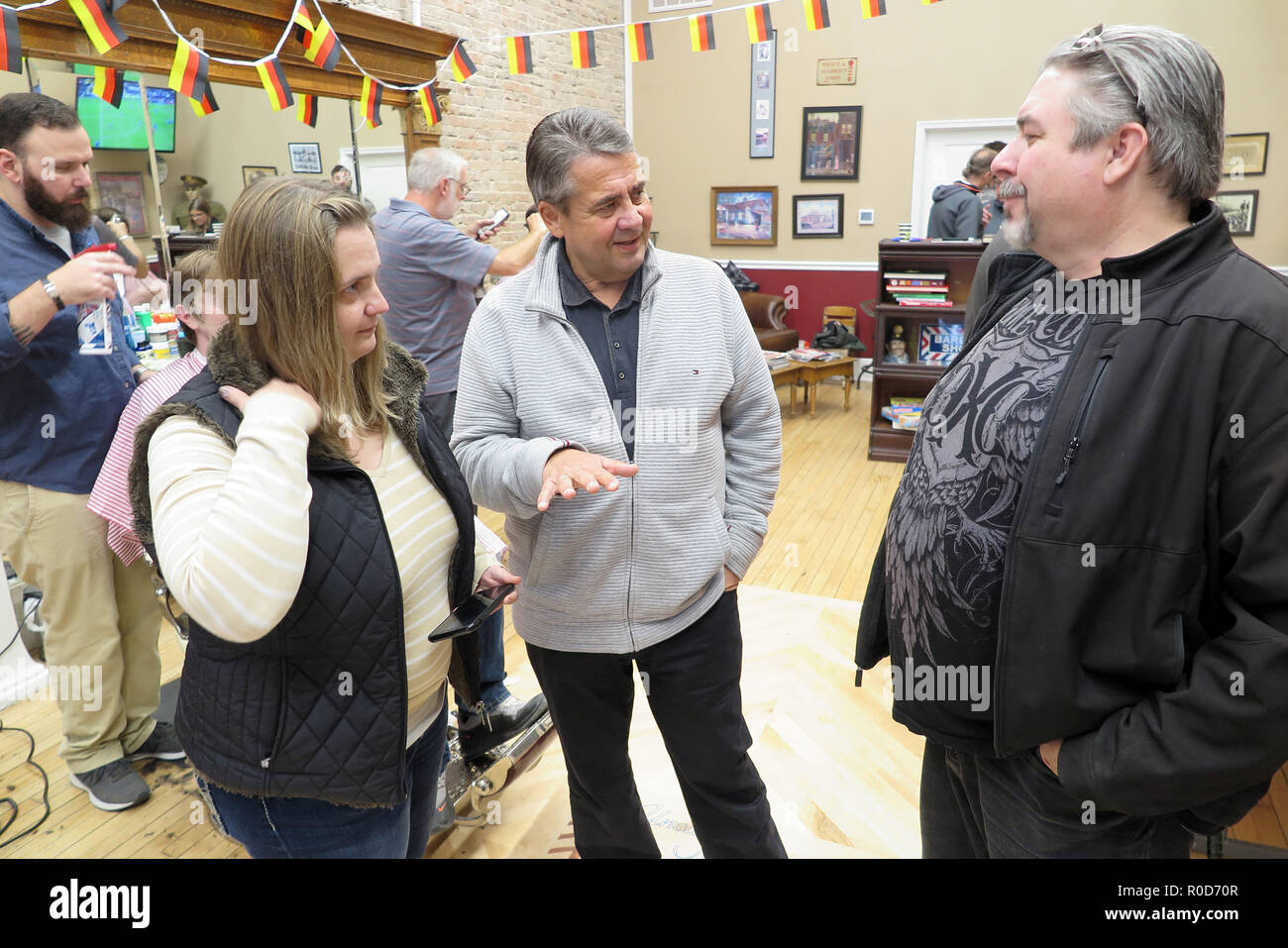 Martinsburg, USA. 03rd Nov, 2018. Former Federal Foreign Minister Sigmar Gabriel (SPD, M) talks to visitors in 'Uncle Joe's Barbershop'. In honour of Gabriel's visit, the owner has hung up small German flags. Gabriel visited the US state of West Virginia, a stronghold of US President Trump. He wanted to talk to the people there to understand why Trump had so much support there. He did it in Uncle Joe's Barbershop, among other places. (to dpa ''Sigmar from Germany'' - Gabriel visiting Trump-Land' from 04.11.2018) Credit: Can Merey/dpa/Alamy Live News Stock Photo