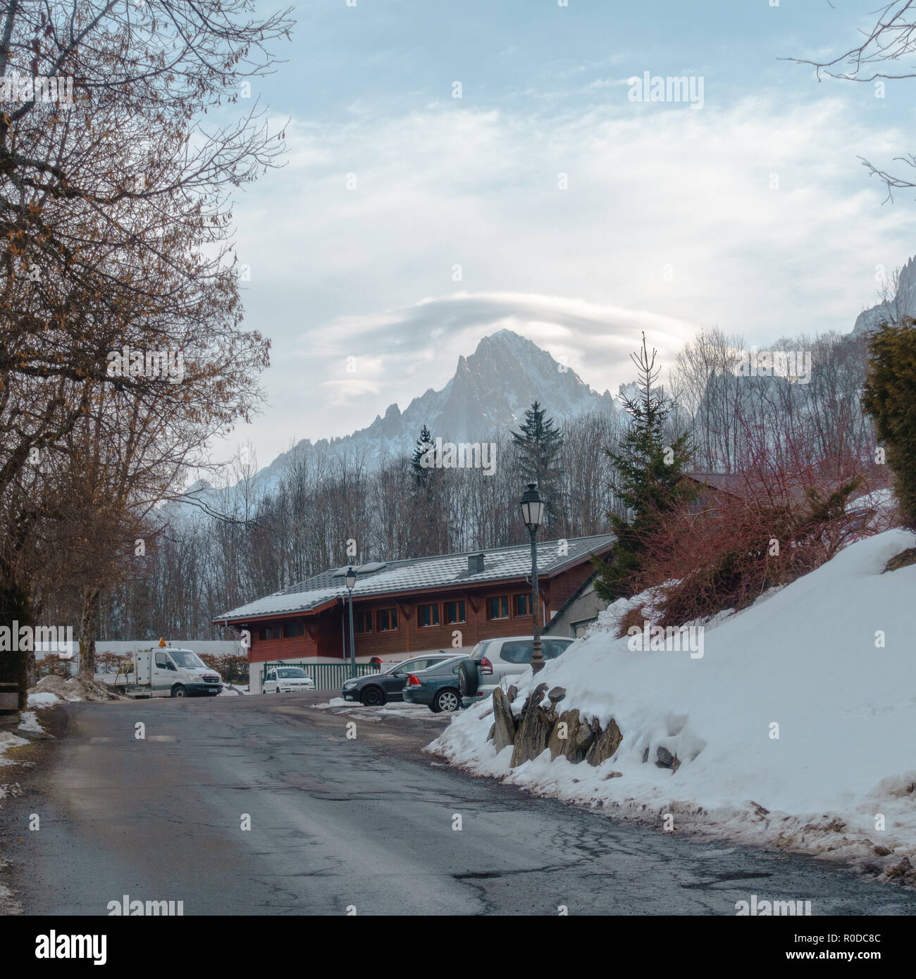 Cracked road, serpentine,  leading to the top of the mountain, houses, cars and a shed, and clouds above mountain top Stock Photo