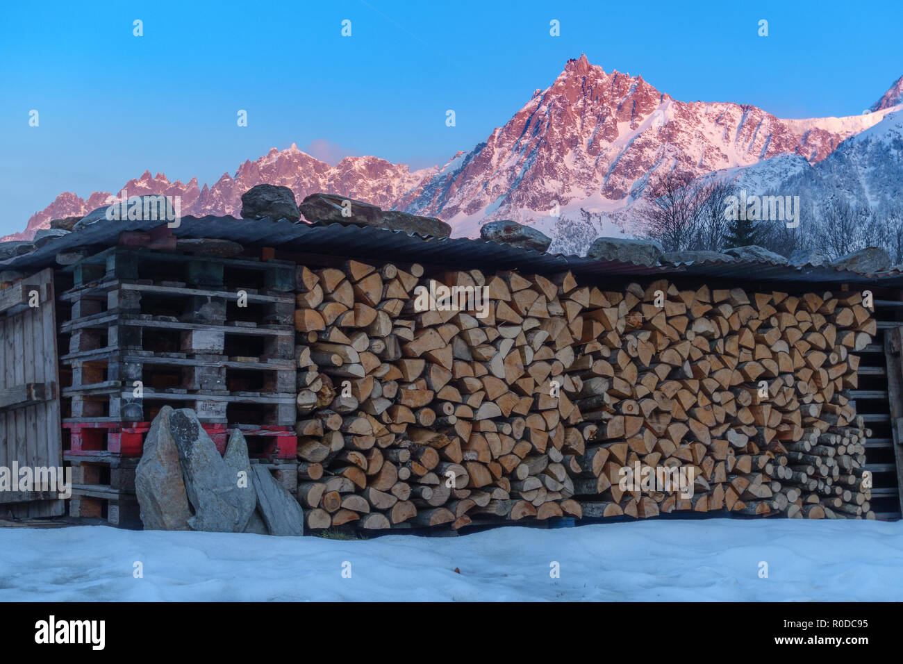 Big red, purple mountain top on sunset and large log store filled with firewood, metal construction Stock Photo