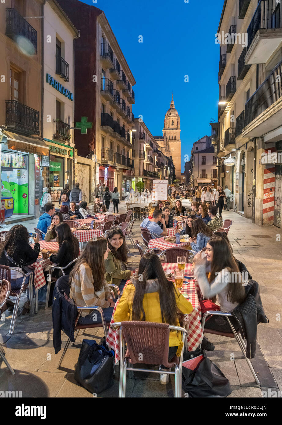 Students at a cafe at night on Calle Rúa Mayor looking towards the tower of the Old Cathedral, Salamanca, Castilla y Leon, Spain Stock Photo