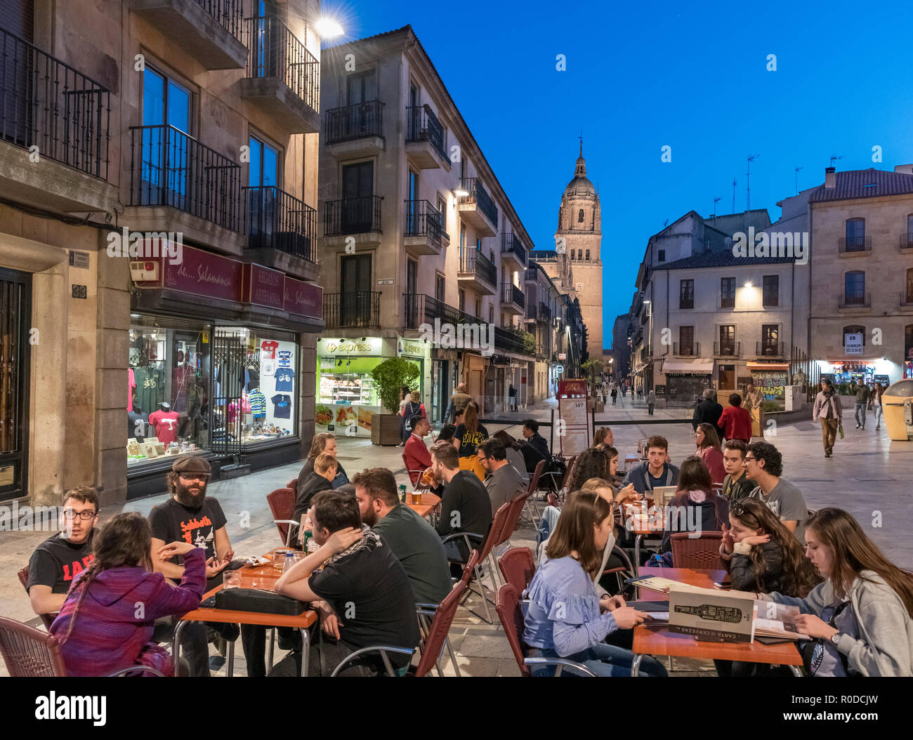 Students at a cafe at night on Calle Rúa Mayor looking towards the tower of the Old Cathedral, Salamanca, Castilla y Leon, Spain Stock Photo