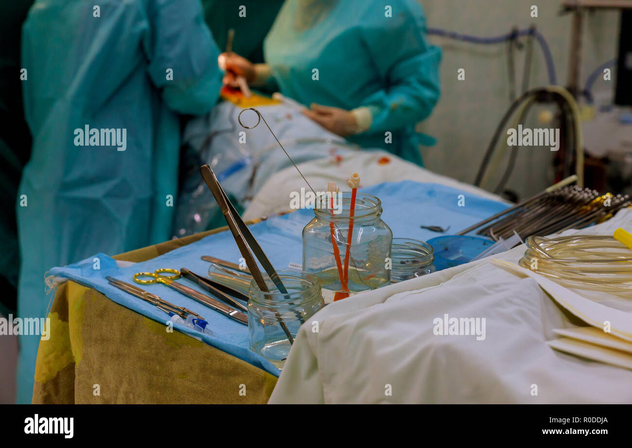 Surgical instruments on table for operation with colleagues performing work in operation room Stock Photo