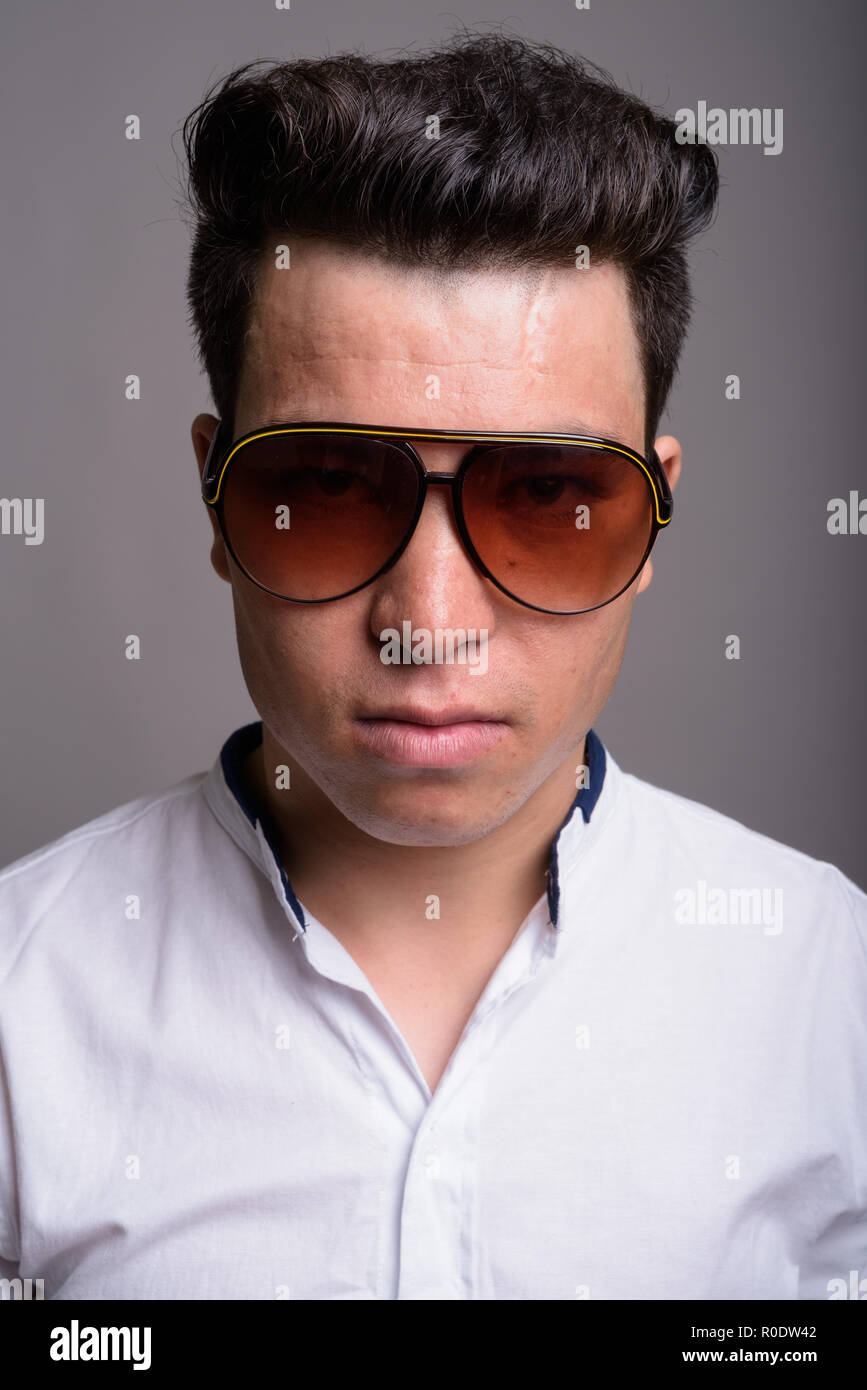 Young Asian businessman wearing sunglasses against gray backgrou Stock Photo