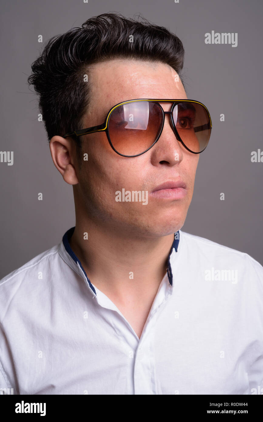 Young Asian businessman wearing sunglasses against gray backgrou Stock Photo