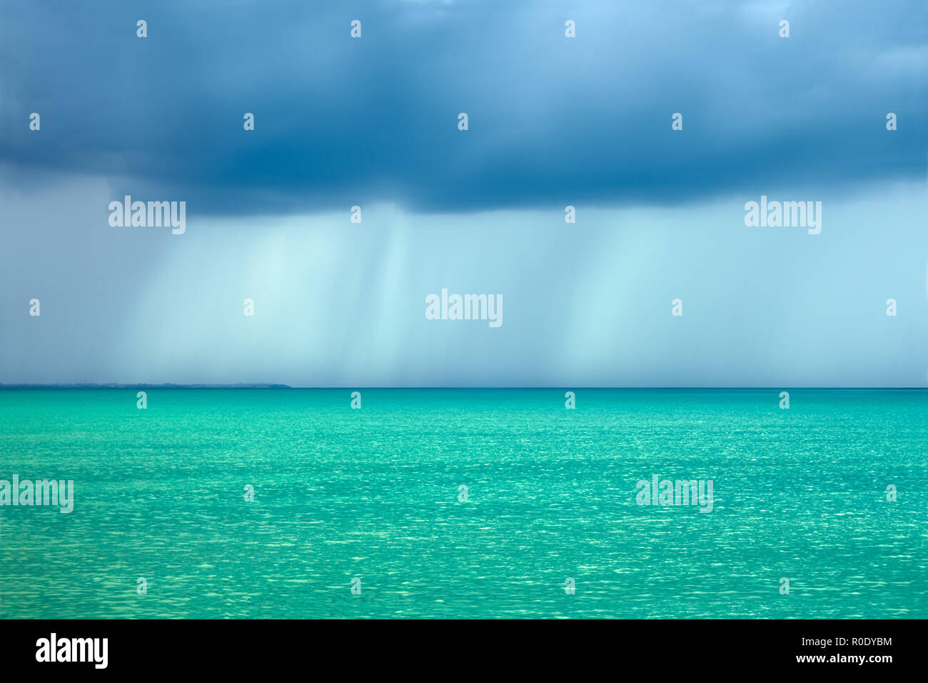 Storm rain clouds over the sea with a turquoise surface illuminated by ...
