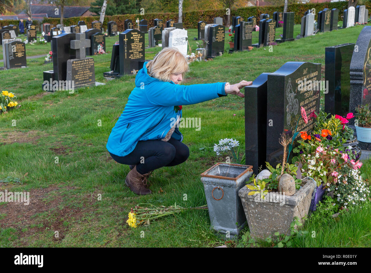 Mature blond lady removes dead flowers from a grave and says a prayer for her father Stock Photo
