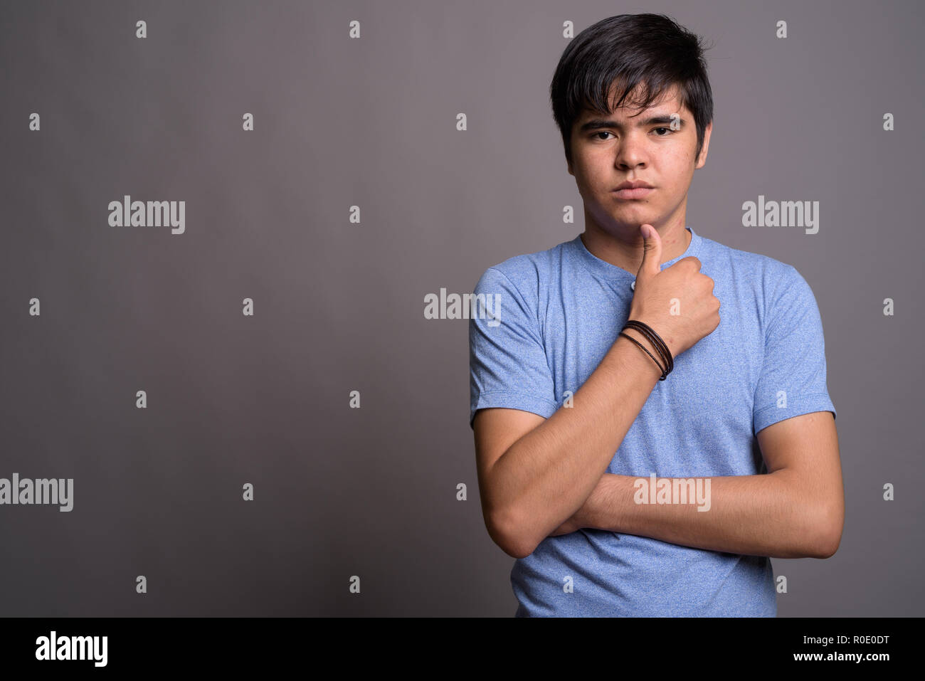 Young Asian teenage boy wearing blue shirt against gray backgrou Stock