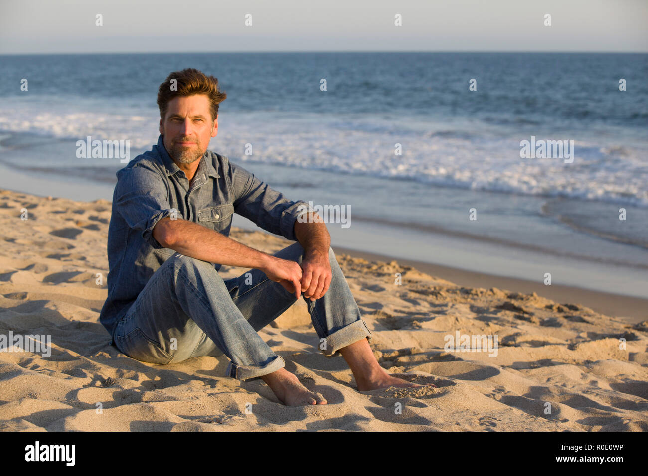 Mid-Adult Man Sitting on Sandy Beach Stock Photo