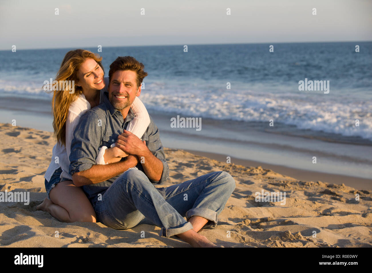 Affectionate Mid-Adult Couple Sitting on Sandy Beach Stock Photo