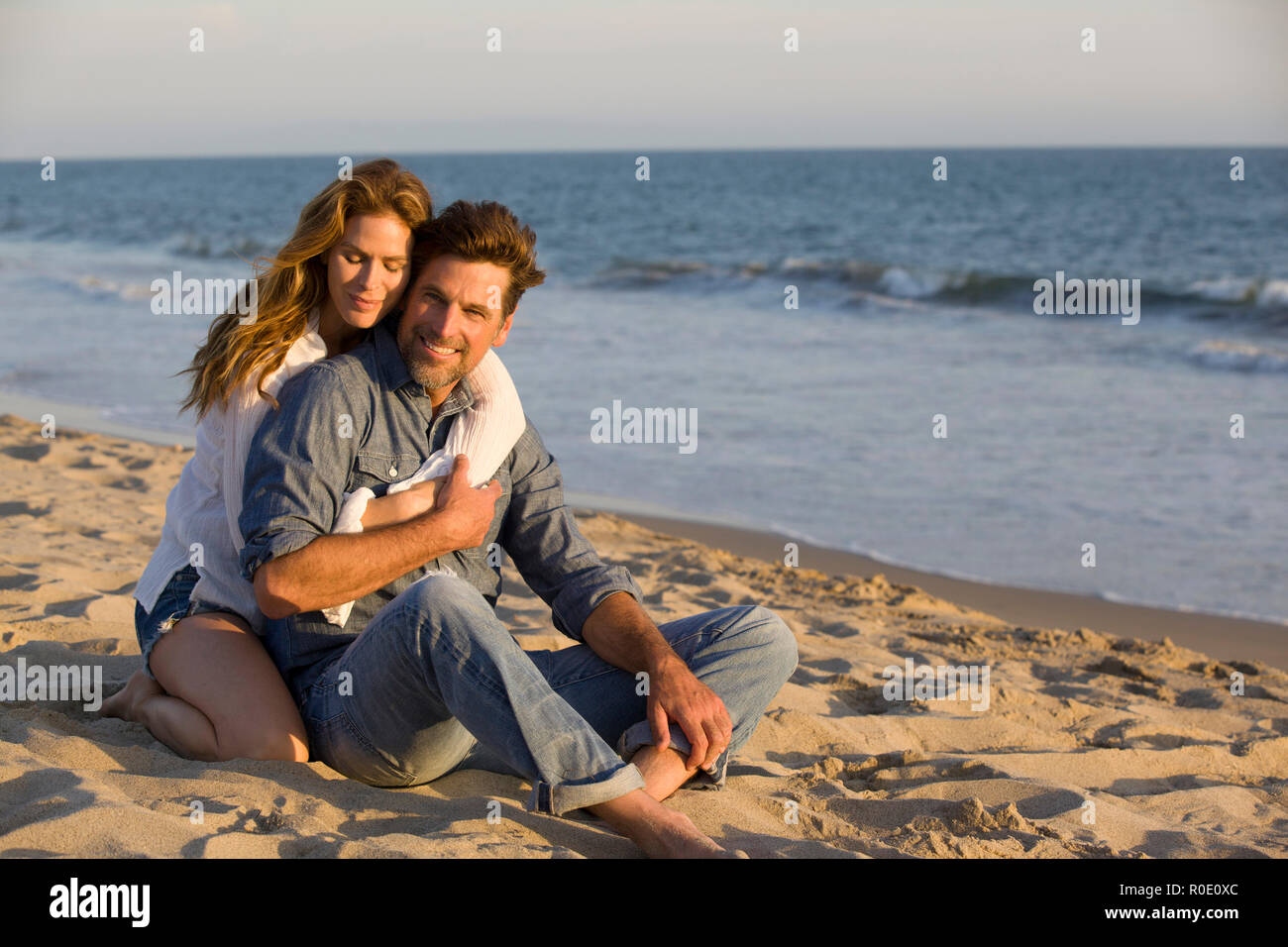 Affectionate Mid-Adult Couple Sitting on Sandy Beach Stock Photo