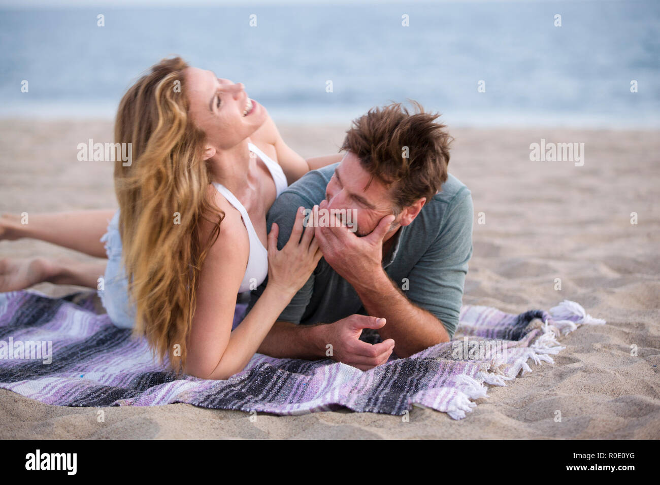 Laughing Mid-Adult Couple Laying on Blanket at Beach Stock Photo