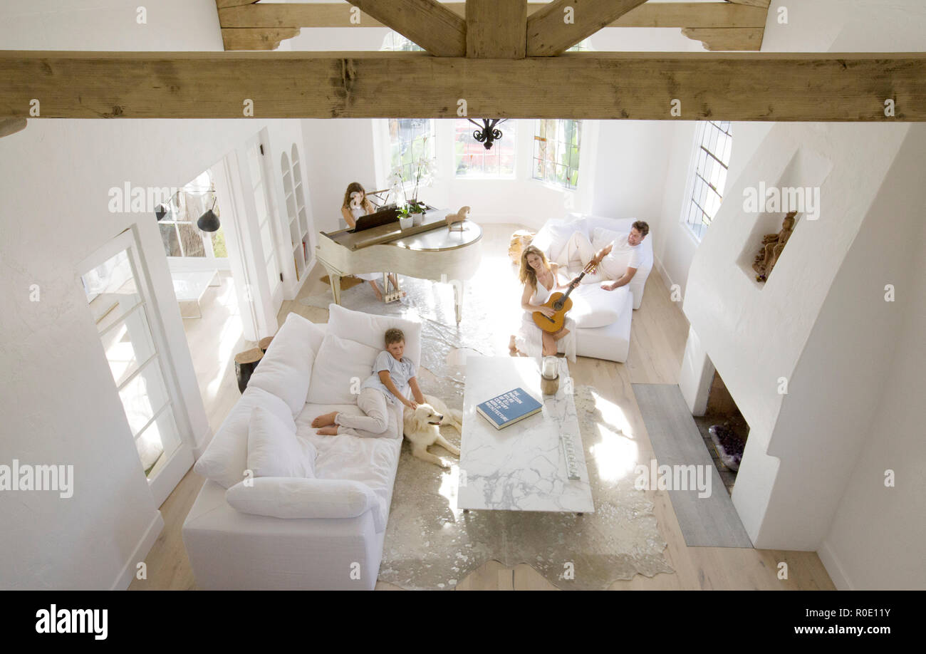 High Angle View of Family and Pet Dog in Living Room, Daughter Playing Piano, Mother Playing Guitar, Father and Son Relaxing on  Sofas Stock Photo