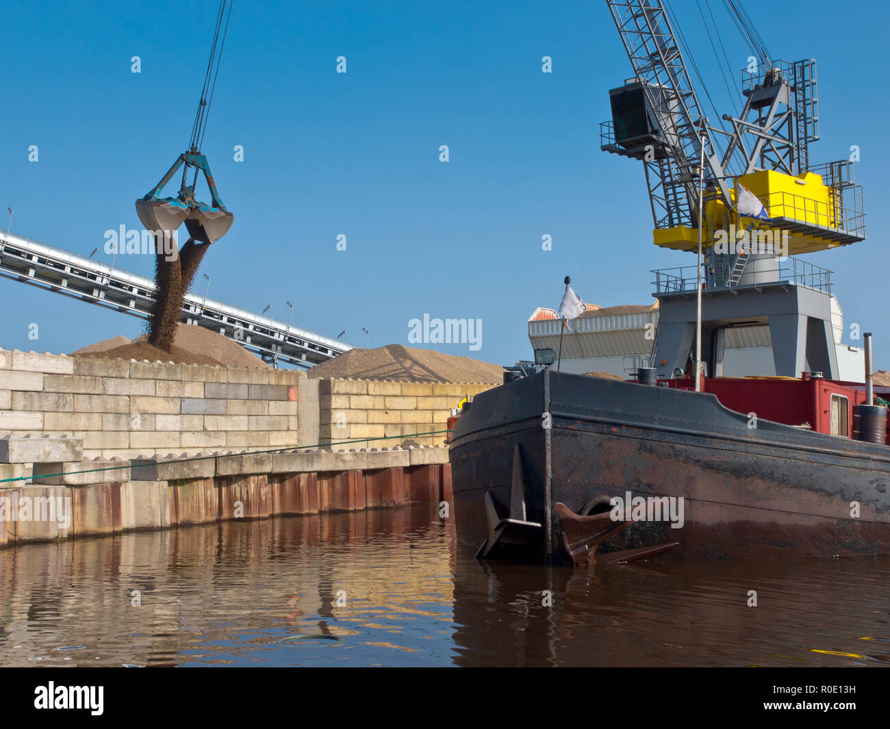 Yellow harbor crane is unloading sand from a ship in a dutch harbor Stock Photo