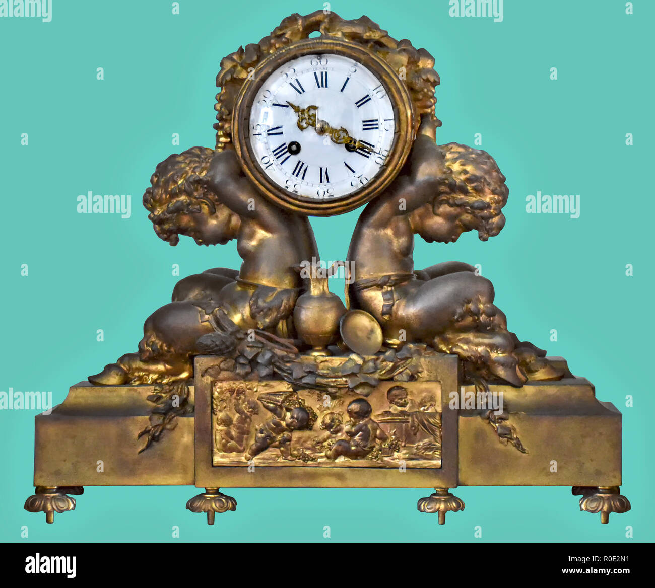 Antique mantel clock of brass children statuettes, on isolated green background with clipping path. Stock Photo