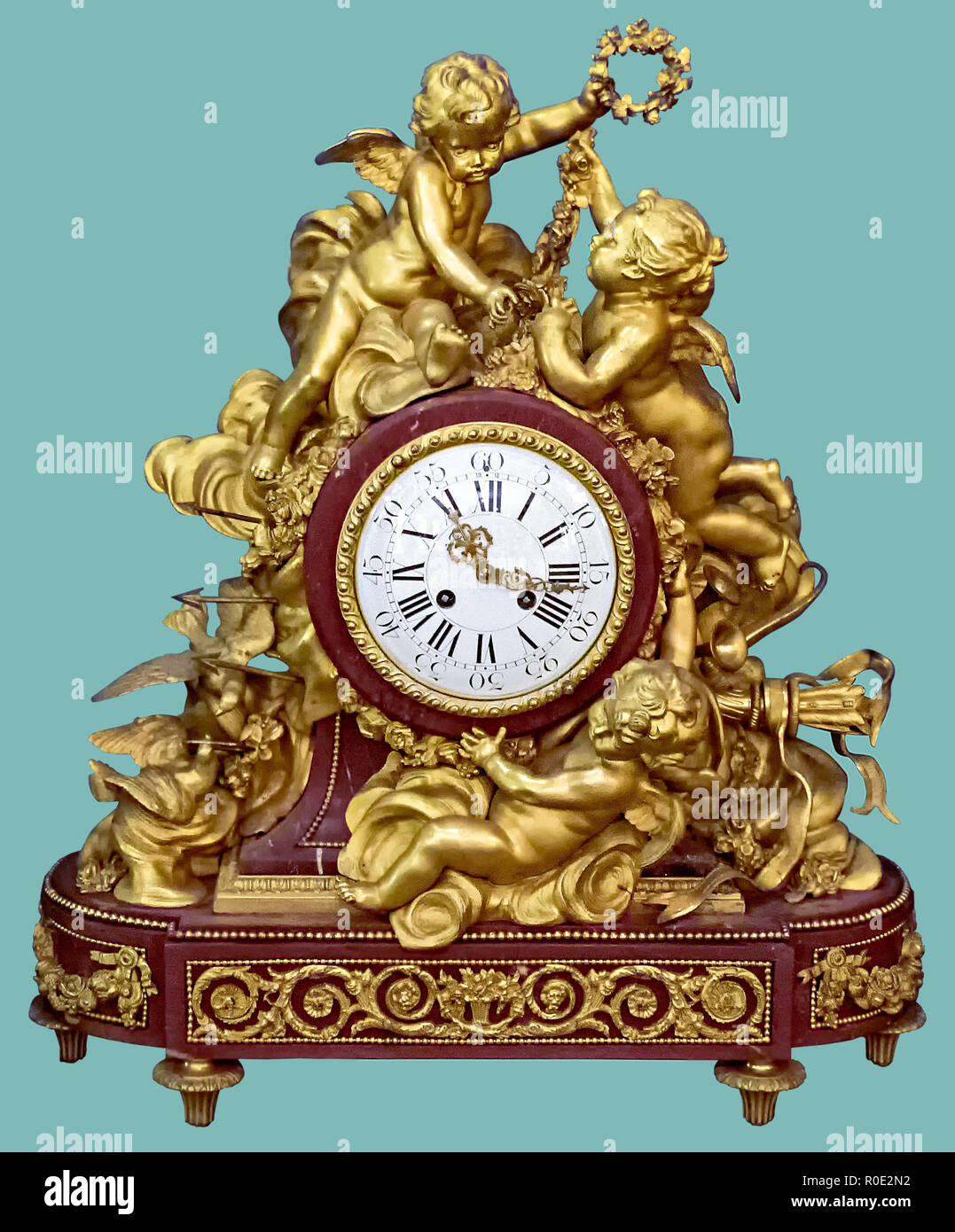 Antique mantel clock of golden cupid and angel statuettes, on isolated green background with clipping path. Stock Photo