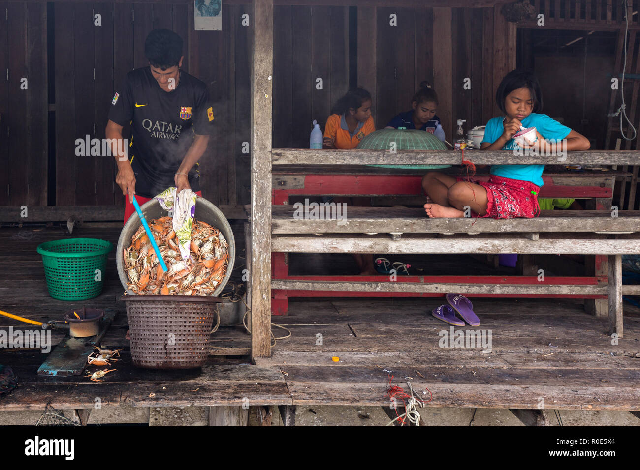 AO YAI, THAILAND, JANUARY 30, 2016 : A man is transferring cooked crabs in a plastic basket while his daughter is sitting and eating an ice-cream in t Stock Photo