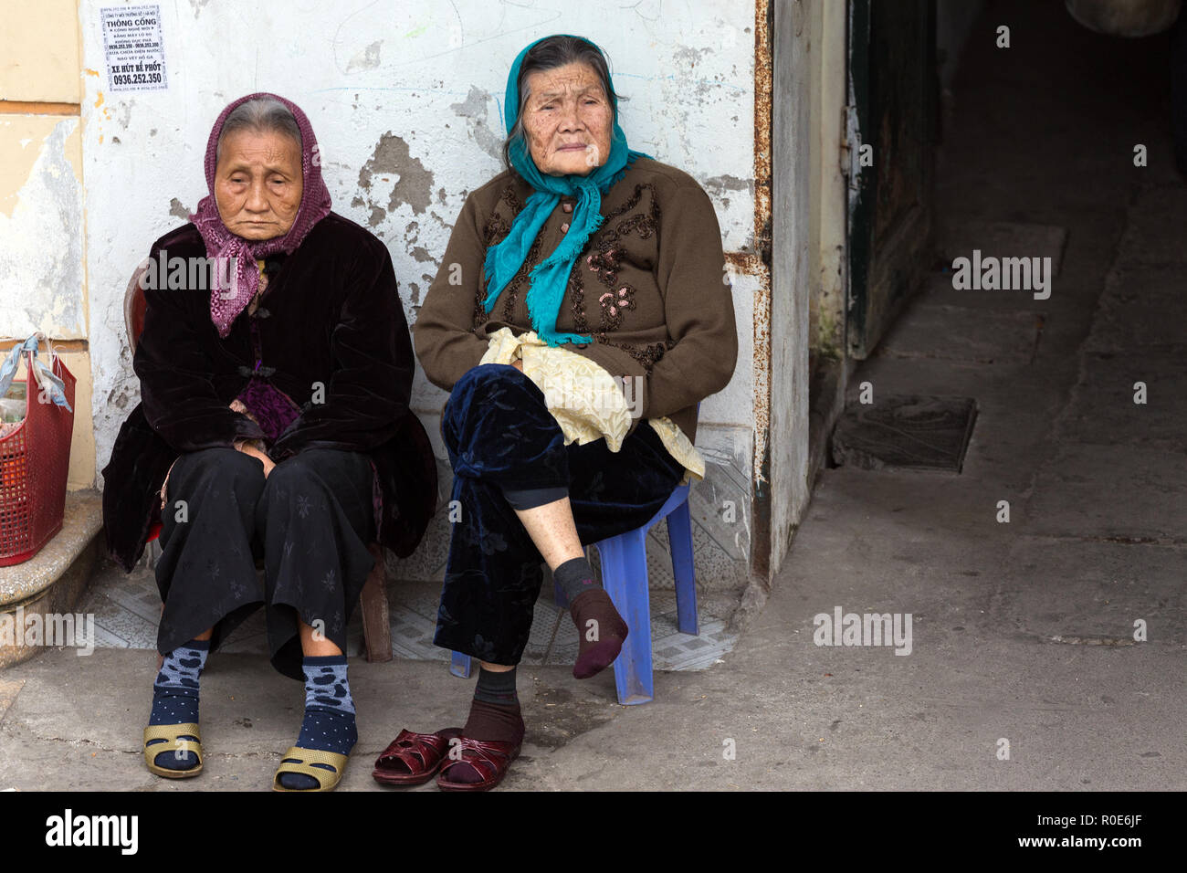 HANOI, VIETNAM, DECEMBER 15, 2014 : Two elderly women are sitting along the street watching the urban life around in Hanoi, Vietnam Stock Photo