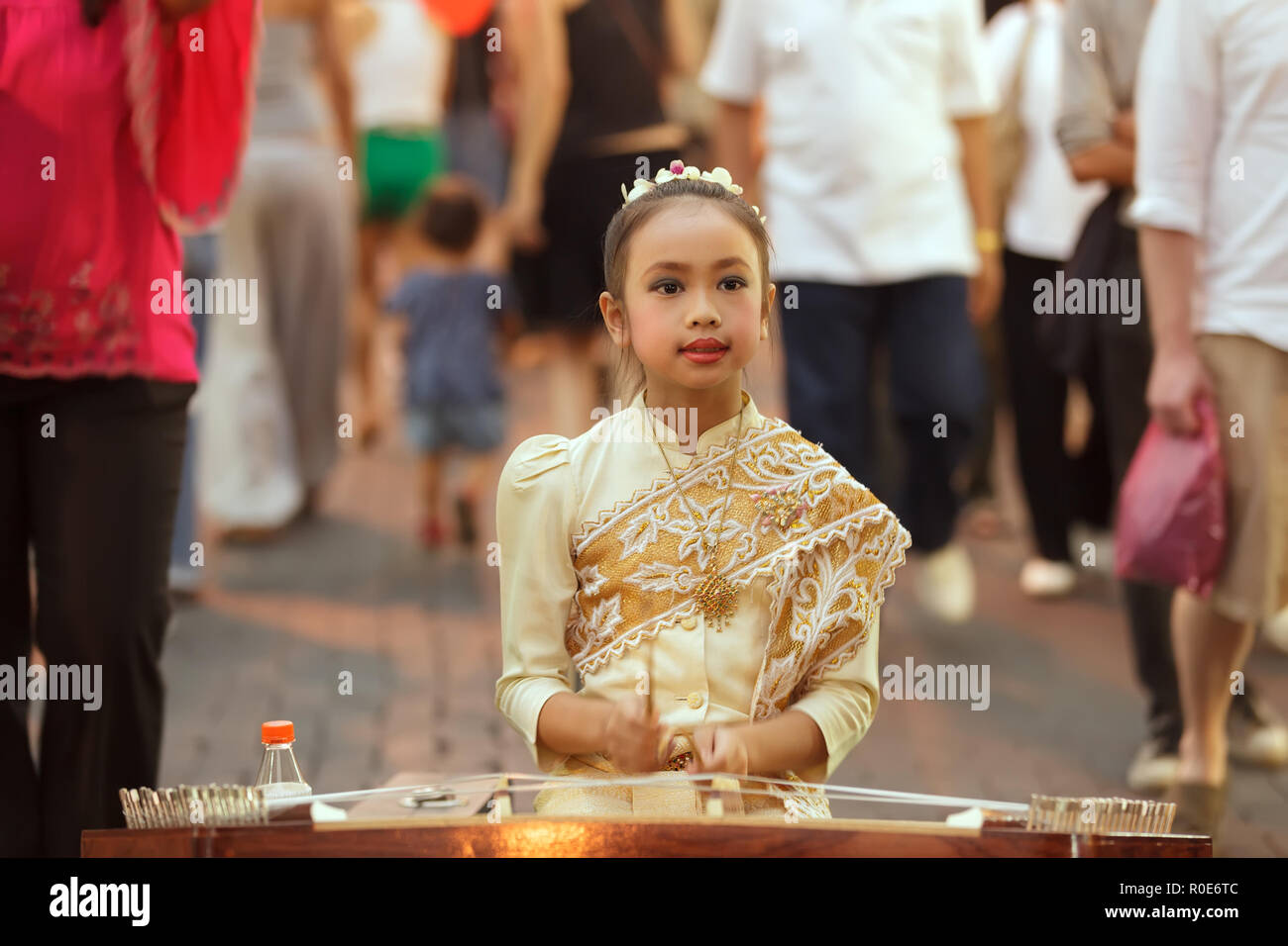 CHIANG MAI, THAILAND, FEBRUARY 26, 2012: A little girl dressed in traditional clothes is playing dulcimer instrument in the street during the week-end Stock Photo